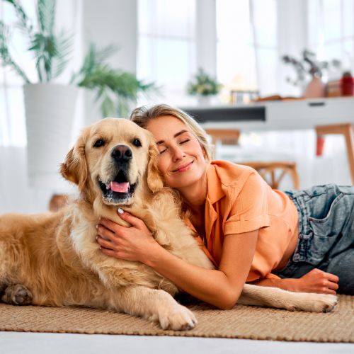 A person lying on the floor hugging a golden retriever dog, both with eyes closed and smiling.